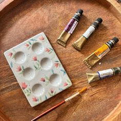 an assortment of paint and brushes sitting on a wooden tray next to some other items