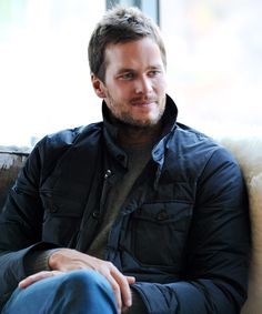 a man sitting on top of a couch in front of a window wearing a black jacket