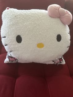 a white hello kitty pillow sitting on top of a red couch with a pink bow