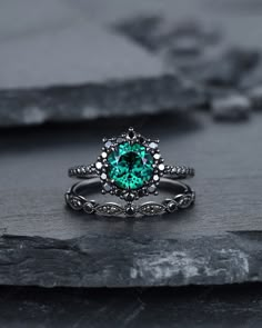 a ring with a green stone in the center on top of a black rock surface