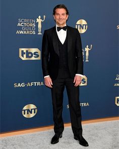 a man in a tuxedo and bow tie standing on a carpet at an awards event