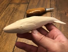 a hand is holding a fake shark toothpick next to a small wooden object