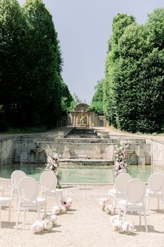 white chairs are set up in front of an outdoor fountain with flowers and greenery