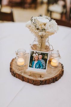 a vase with flowers and candles is on a wooden slice at the center of a table