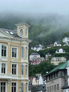 the fog is rolling in from the mountains behind some buildings and houses on a hill