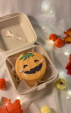 a cupcake in a box with a face drawn on it, surrounded by fall leaves