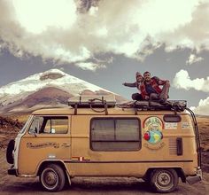 two people sitting on top of an old van in front of a snow covered mountain