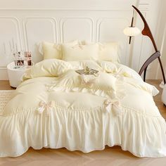 a white bed with ruffles and pillows on it in a room next to a lamp