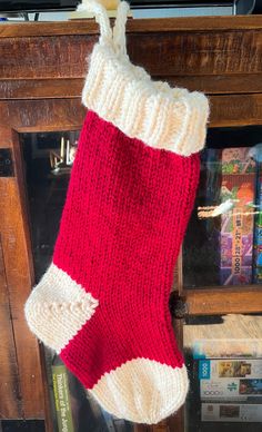 a red and white knitted christmas stocking hanging from a wooden pole in front of a fireplace