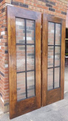 two wooden doors sitting side by side next to a brick building with windows on each side