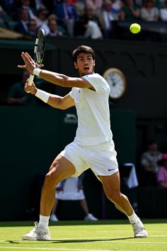 a man swinging a tennis racquet at a ball on a court with spectators in the background