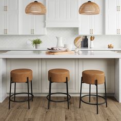 three stools sit at the center of a kitchen island with white cabinets and wood flooring