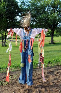 a child's scarecrow is standing in the dirt wearing overalls and headdress