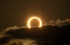 the solar eclipse is seen through clouds as it passes in front of an object that looks like a ring