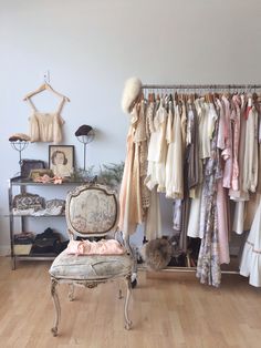 an old chair sits in front of a rack of dresses and other clothing on hangers