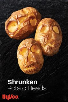 three baked potatoes with faces carved into them on a black stone surface, the words shrunken potato heads