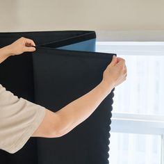 a person holding up a black piece of material in front of a window with white curtains