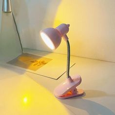 a pink desk lamp sitting on top of a white table next to a yellow light