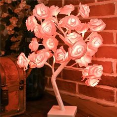 a white vase with pink roses in it next to a red brick wall and trunk