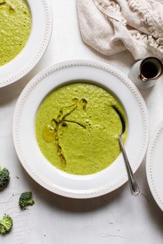 two white plates topped with soup next to broccoli