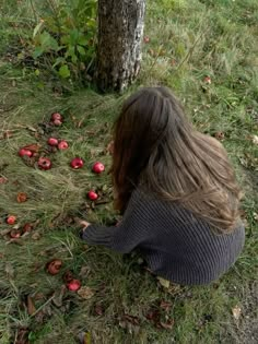 a woman sitting on the ground next to a tree with apples all over her face