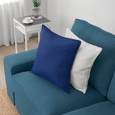 a blue couch with two white pillows and a small table in the corner behind it