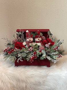 a christmas arrangement in a red box on a white furnishing with poinsettis and greenery