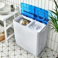 a white and blue washing machine sitting on top of a tiled floor next to a potted plant