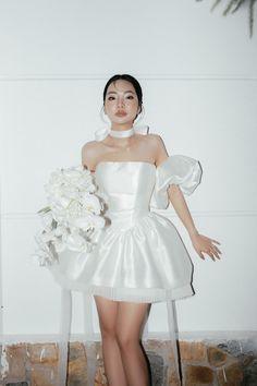 a woman in a white dress holding a bouquet of flowers and posing for the camera