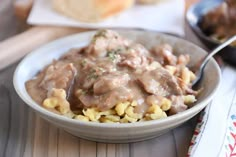 a white bowl filled with pasta and meat covered in gravy on top of a wooden table