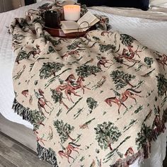 a bed with a blanket on top of it next to a night stand and candle