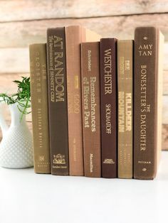 four books are lined up next to a white vase