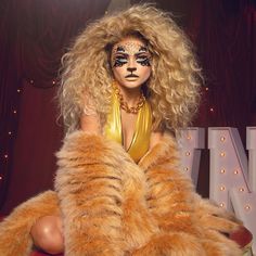 a woman with long blonde hair sitting on top of a red chair wearing a gold outfit