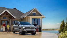 two people standing in front of a house with a silver suv parked next to it