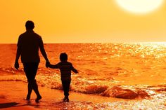 a father and son walking on the beach with an orange sunset in the back ground