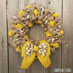 a burlap wreath with yellow and brown bows hanging on a wooden wall next to a fence