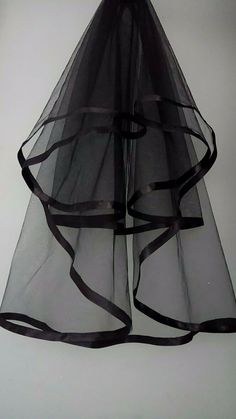 a black veil hanging from the ceiling in front of a white wall with ribbon on it