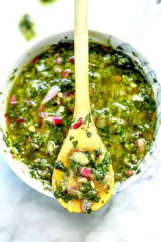 a wooden spoon filled with green soup on top of a table