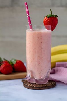 a smoothie with strawberries on the side and two bananas in the background next to it