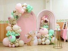 balloons and decorations are arranged on the floor in front of a pink arch with bunny ears