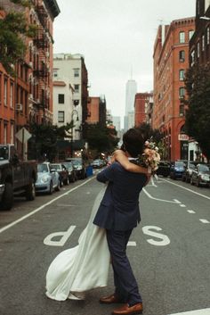 a bride and groom hugging in the middle of an empty street with cars parked on both sides