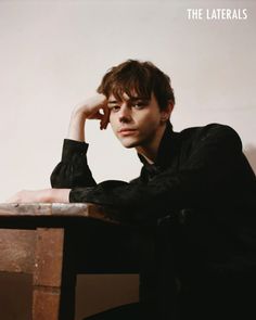 a young man sitting at a table with his hand on his head and looking off to the side