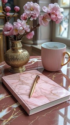 a pink marbled table topped with a gold vase filled with flowers and a notebook