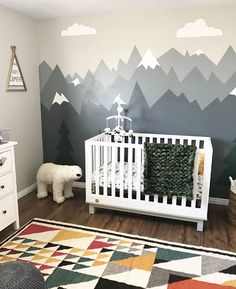 a baby's room with mountains painted on the wall and a white crib