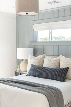 a bed with white sheets and pillows in a bedroom next to a window that has blue paneling on the walls