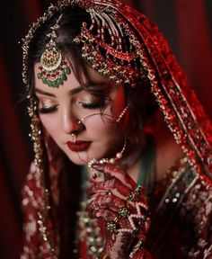 a woman in red and gold is dressed up for her wedding day, with jewelry on her face