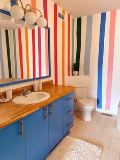 a bathroom with multicolored stripes painted on the walls and wooden counter tops, along with a toilet