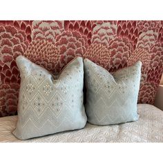 two decorative pillows sitting on top of a bed next to a red and white wall