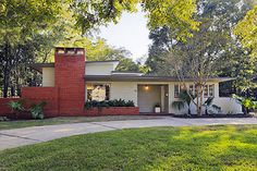 a small brick house in the middle of a yard with trees and grass around it