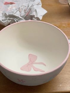 a pink and white bowl sitting on top of a wooden table next to tissue paper